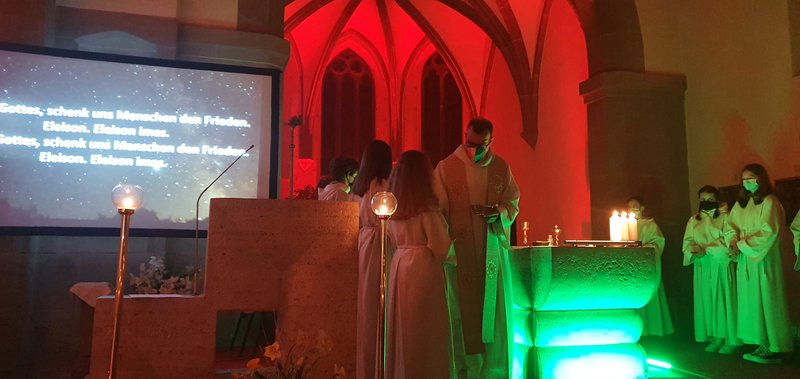 In der bunt beleuteten Kirche helfen Messdiener die  Gaben zum Altar zu bringen.